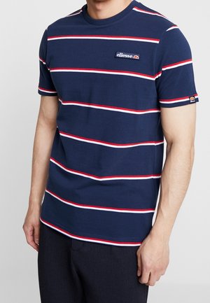 Mężczyzna w granatowym t-shircie z poziomymi czerwono-białymi paskami oraz logo ellesse na piersi i rękawie.