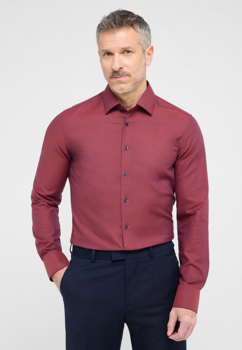 Bordeaux kleurig langarmen shirt met een gestructureerde stof, button-down kraag en marineblauwe knopen. Gecombineerd met marineblauwe broek, slim fit ontwerp.