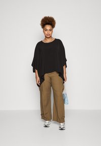 Black, flowy top with short sleeves; paired with loose, khaki cargo pants. Accessories include a light blue handbag and silver sneakers.