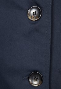 Tela azul marino con un acabado texturizado que presenta dos botones negros brillantes, cada uno con cuatro orificios y un diseño circular.