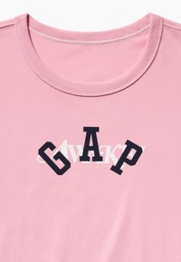 Ροζ μπλουζάκι με στρογγυλή λαιμόκοψη με επικαλυπτόμενα μαύρα και λευκά γράμματα που σχηματίζουν το «GAP» στο στήθος.