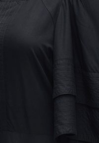 Gros plan d'un vêtement noir avec des coutures détaillées sur la manche et un design de tissu superposé.