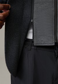 Czarna kurtka o fakturze z ciemnego materiału z szarym wykończeniem z polaru w środku, z zamkiem błyskawicznym. Czarne spodnie z widocznym guzikiem i kieszenią poniżej.