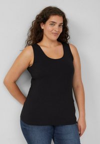 Schwarzes ärmelloses Tanktop aus Baumwolle, mit rundem Halsauschnitt und lockerem Schnitt, kombiniert mit blauer Jeans.