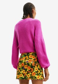 Fuksia neulepusero, jossa on pallohihaiset ja lyhyt malli. Yhdistetty värikkääseen kukalliseen minihameeseen, jossa on keltaisia ja oransseja kukkia.