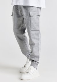 Grå sweatpants med sidelommer, tætsiddende ben og en blød tekstur. Kombineret med hvide sneakers med en klodset sål.