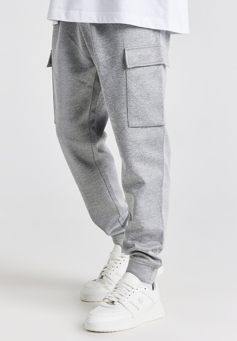 Grå sweatpants med sidelommer, tætsiddende ben og en blød tekstur. Kombineret med hvide sneakers med en klodset sål.