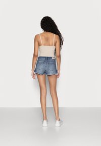 Top corto beige de canalé con tirantes finos combinado con pantalones cortos de mezclilla azul claro con dobladillo deshilachado y bolsillos traseros. Se lleva con zapatos blancos sin cordones.