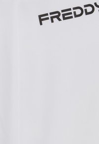 Valkoinen kangas, jossa on sileä pinta, ja yläosassa on paksulla mustalla kirjasimella painettu sana "FREDDY".