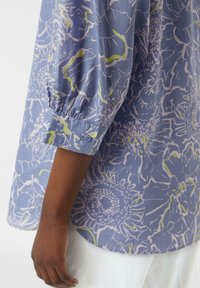 Floral-patterned blouse in light blue fabric with green and white accents. Features puffed sleeves and buttoned cuffs. Smooth texture.