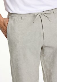 Ljust grå linbyxor med en elastisk midja och dragsko samt sidfickor, som visar en texturerad tygfinish.
