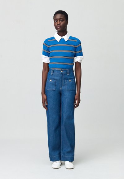 Top en tricot rayé bleu avec col blanc, associé à un pantalon en jean large taille haute avec poches avant. Des baskets blanches complètent la tenue.