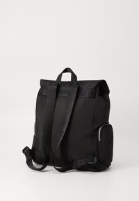 Black fabric backpack with adjustable straps, roll-top closure, side zip pocket, and branded webbing accents. Smooth texture, minimalist design.