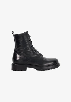 Botte de combat noire en cuir avec lacets, à semelle en caoutchouc épaisse et tirant au talon, présentée de côté sur fond blanc.
