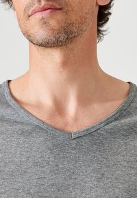 T-shirt grigio a coste con scollo a V realizzato in tessuto morbido. La maglietta presenta una forma classica con un scollo basso e dettagli minimi.