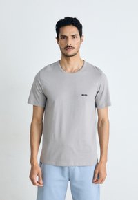 T-shirt gris à manches courtes en coton, avec un col rond et un petit logo noir "BOSS" au-dessus de la poitrine gauche. Associé à un pantalon bleu clair.