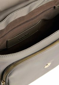 Vista interna di una borsa beige che mostra la fodera in tessuto Marrone, una tasca con zip e un comparto frontale con zip dorata e chiusura magnetica.