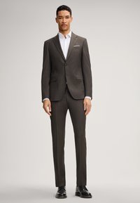 Completo marrone scuro con vestibilità su misura, dotato di giacca a due bottoni, revers a navetta e pantaloni abbinati. Camicia bianca fresca sotto.