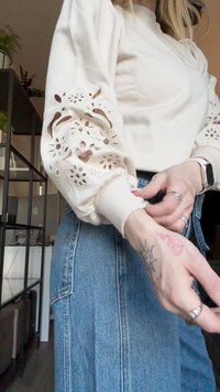 Felpa bianca con dettagli floreali intagliati sulle maniche, polsini a costine, abbinata a jeans in denim a vita alta e vestibilità rilassata.