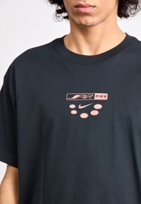 Sort bomulds T-shirt med et pink "Air Max" logo og prikker. Korte ærmer, rund halsudskæring og afslappet pasform. Glat tekstur.