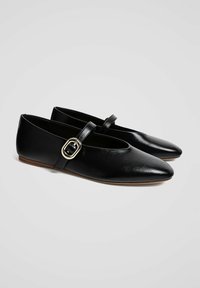 Ballerine in pelle nera con punta affusolata, dotate di una tracolla con una fibbia quadrata in argento. Texture liscia e suola bassa e flessibile.