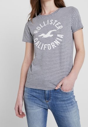 T-shirt à rayures grises et blanches, à manches courtes et col rond, avec un logo circulaire Hollister California au centre.