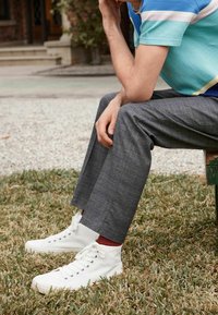 Baskets montantes blanches, pantalon à carreaux gris et chemise rayée turquoise. Le tissu est lisse avec des motifs et une texture visibles.