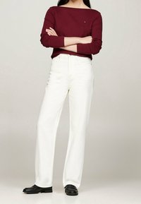 Top lungo bordeaux con scollo a barca abbinato a jeans bianchi a gamba larga e scarpe nere. Materiale in cotone morbido, design semplice.