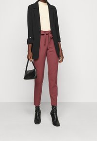 Černý blazer, krémový top, burgundské kalhoty s mašlí na opasku, černá strukturovaná kabelka a špičaté černé kotníkové boty. Hladké textury po celou dobu.