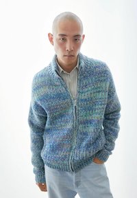 Gestructureerde gebreide cardigan in blauwtinten en groentinten, voorzien van een ritssluiting en een gestructureerde kraag. Gecombineerd met lichtblauwe spijkerbroek.