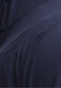 Gros plan d'un tissu bleu marine montrant des coutures détaillées et des coutures sur un vêtement, probablement une veste ou un manteau.