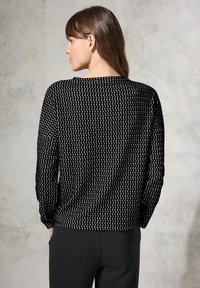 Schwarzer und weißer gemusterter Pullover mit wellenförmigem Design, langen Ärmeln und geräumiger Passform. Der Rücken hat einen runden Ausschnitt und strukturierten Stoff.