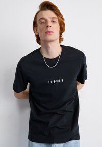 Juodas medvilnės marškinėliai su apvalia iškirpte ir baltu "JORDAN" tekstu priekyje, su trumpomis rankovėmis ir laisvu kirpimu.