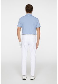 Męski strój golfowy składający się z jasnoniebieskiej koszulki polo i białych spodni. Rękawica na lewej ręce, sporty buty widoczne na dole.