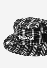 Chapéu balde em padrão xadrez preto e branco, com uma coroa arredondada, aba larga e logotipo bordado "wastedparts" na frente.