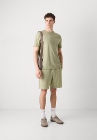Light green cotton t-shirt with embossed logo, paired with matching shorts. Model wearing brown crossbody bag and gray sneakers.
