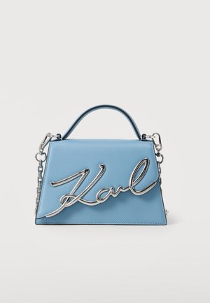 Svetlomodrá kabelka v tvare lichobežníka s vrchnou rukoväťou, strieborným reťazovým popruhom a veľkým strieborným kurzívnym nápisom "Karl" na prednom chlopni.
