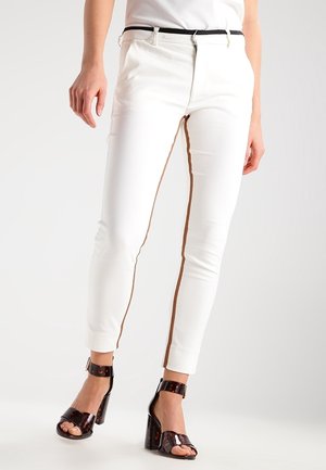 Pantalones ajustados blancos con una franja lateral marrón, hechos de una tela suave. Combinados con sandalias de tacón glossy en marrón oscuro.