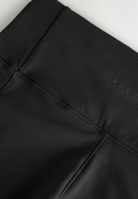 Nærbillede af sorte high-waist leggings, der viser forstærket syning og et subtilt præget mærkelogo på det glatte stof.