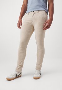 Beige corduroy pants with a slim fit, featuring a button closure and pockets, worn with white sneakers and a light blue t-shirt.