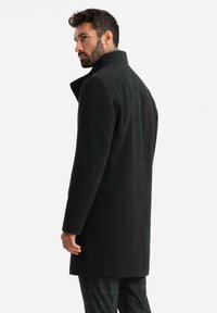 Abrigo de lana negro con cuello alto y corte entallado. Presenta una textura suave y un corte recto hasta la mitad del muslo.
