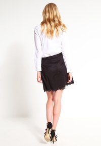 Svart kjol med vågig spetsdekoration, tillverkad av ett mjukt tyg. Bärs tillsammans med en vit skjorta med knappar, vilket ger en avslappnad men ändå skräddarsydd look.