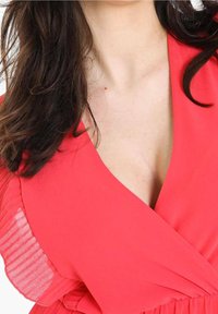 Robe portefeuille corail avec des accents plissés le long des épaules, dotée d'un col en V profond pour une silhouette définie. Texture de tissu lisse.