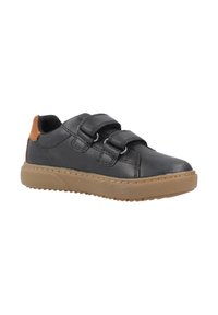 Zapatilla de cuero negra con talón marrón, dos correas de velcro y una gruesa suela de goma marrón clara, vista de lado.