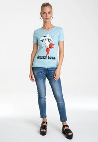 Light blue t-shirt featuring a graphic of a cartoon cowboy with a red bandana, paired with fitted blue jeans and black platform sandals.