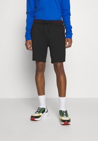 Shorts noirs avec taille à cordon de serrage et poches avec accents rouges, associés à des baskets colorées et à une chemise bleu à manches longues.