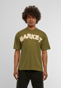 Camiseta de algodón verde oliva con mangas cortas y cuello redondo, que presenta la palabra "MARKET" en grandes letras color crema en el pecho.