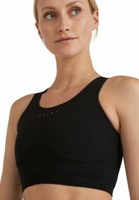 Czarny sportowy biustonosz z prążkowaną fakturą, z okrągłym dekoltem i subtelnym czerwonym logo. Gładki materiał i dopasowany krój zapewniający wsparcie.