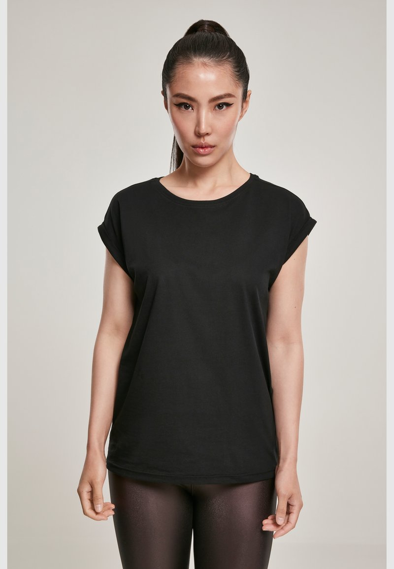Tricou negru dintr-un material moale din bumbac, cu mâneci scurte răsucite și decolteu rotund, asortat cu colanți negri lucioși.