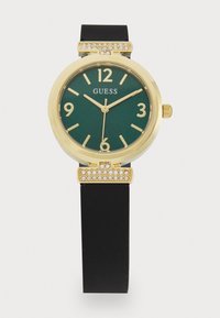 Montre dorée avec un cadran vert, bracelet en silicone noir, accessoires ornés de cristaux, grands chiffres et verre minéral.